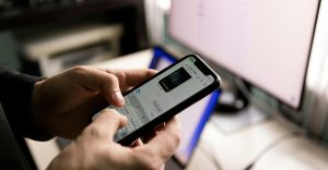 Persona escribiendo un mensaje de WhatsApp en el móvil frente al ordenador